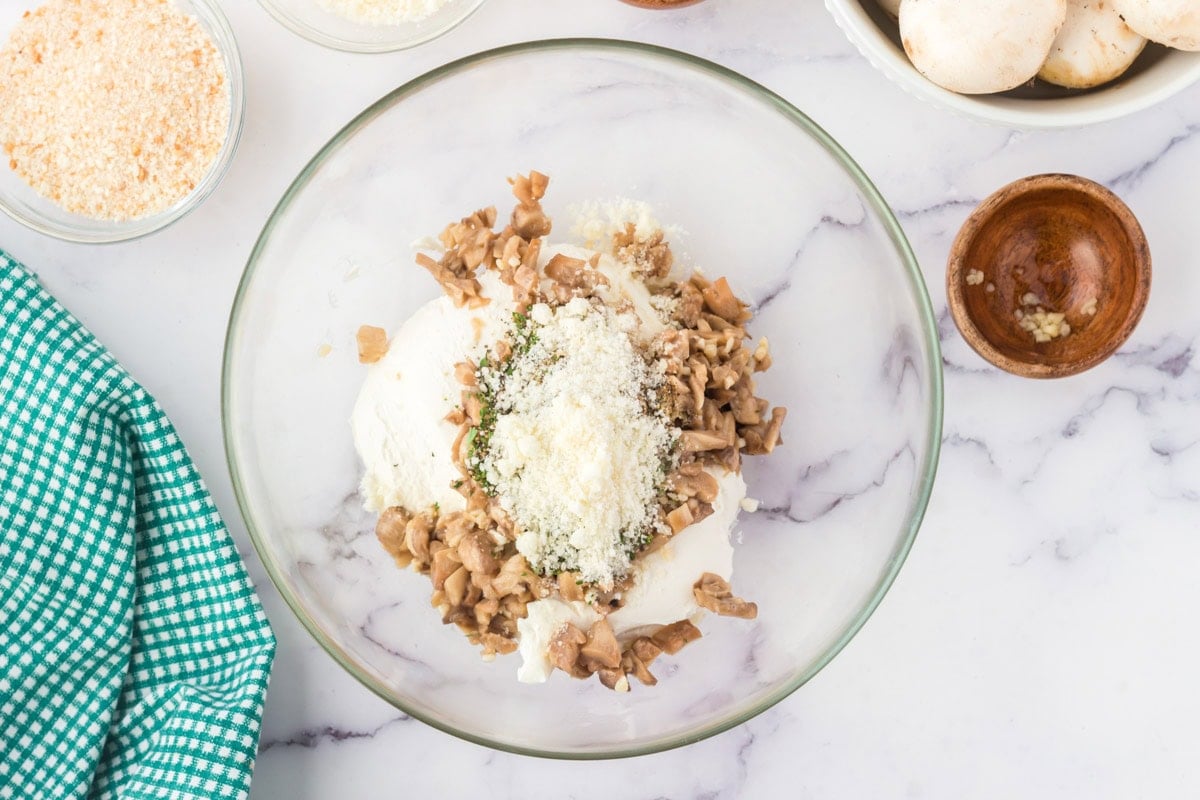 Cheese and chopped sauteed mushrooms in a glass bowl.