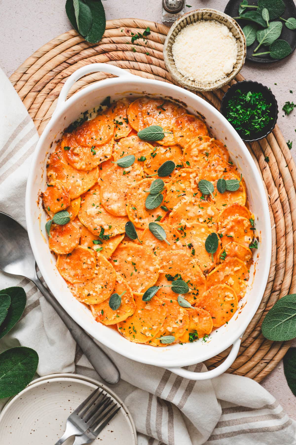 Baked sweet potato gratin in a white casserole dish with fresh sage leaves on top.