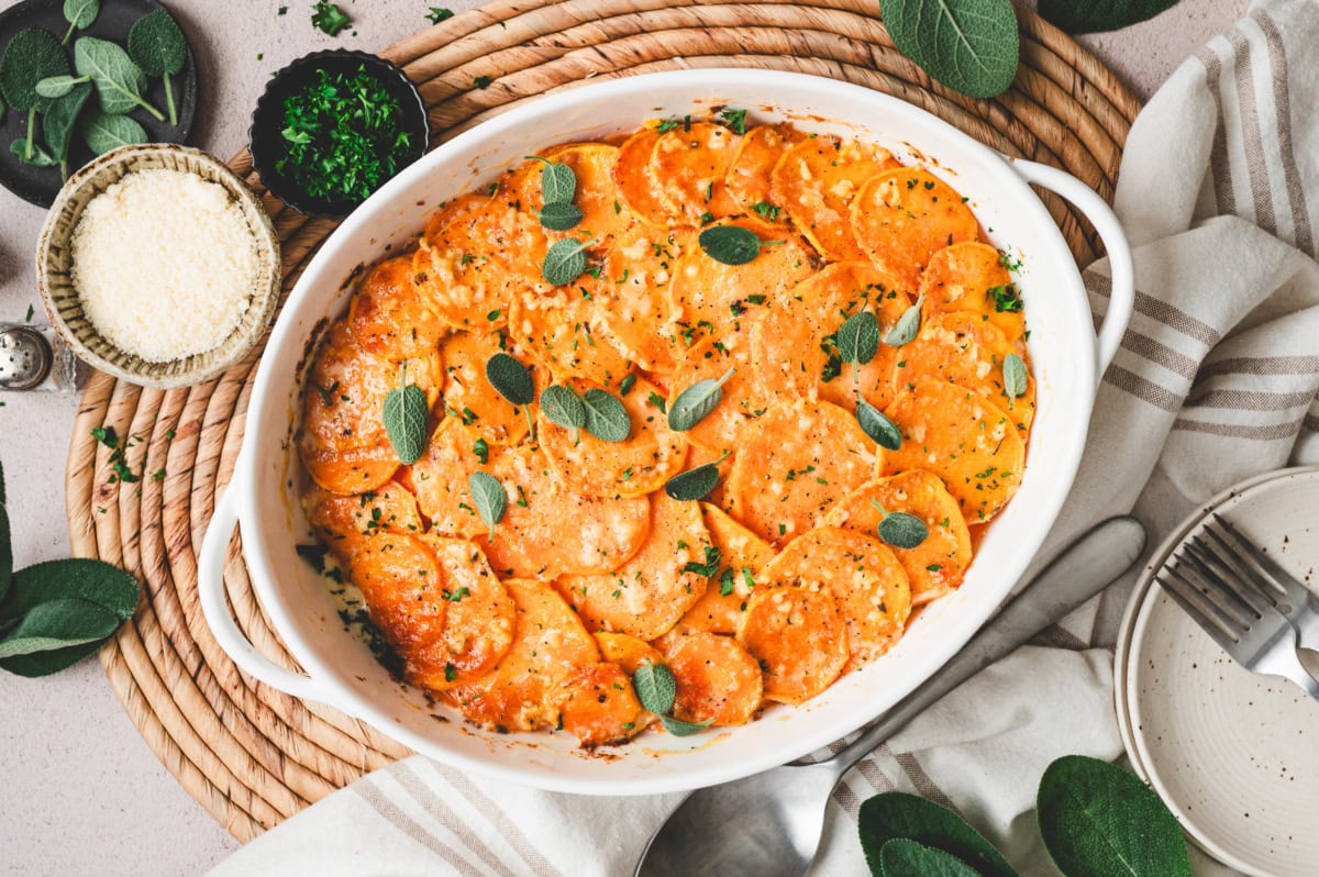 Sweet potato gratin in a white casserole dish, garnished with fresh sage leaves.