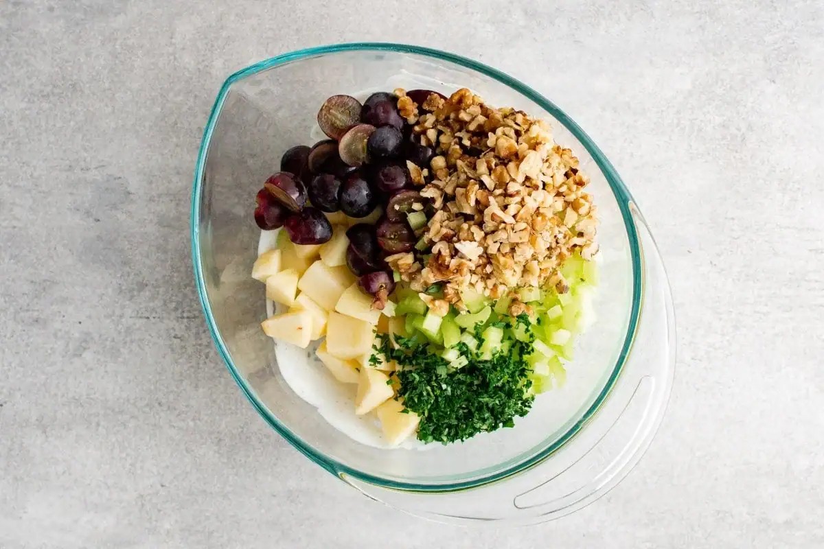 sliced grapes, chopped apples, walnuts, celery and parsley in a clear glass bowl.