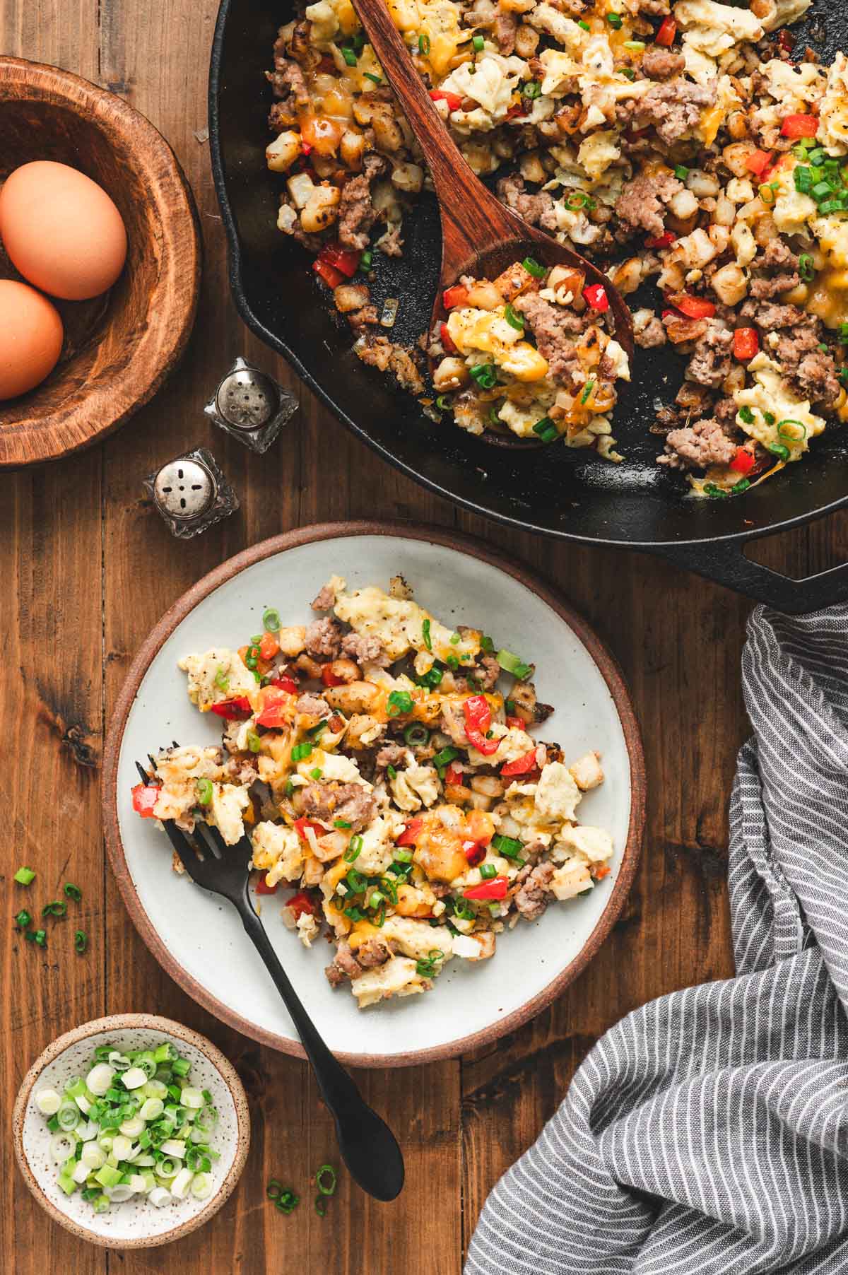 Breakfast hash in a cast iron skillet next to a ceramic plate with breakfast hash and a fork.