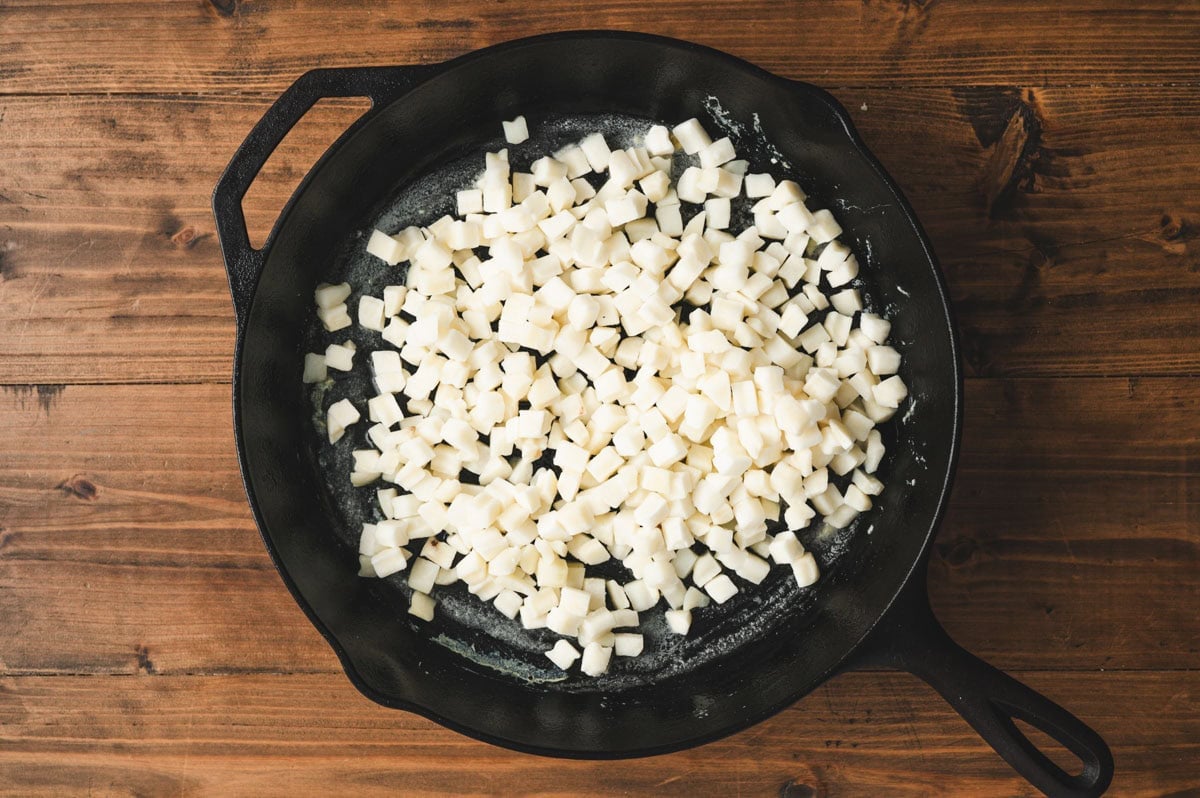Uncooked diced potatoes in a cast iron skillet.