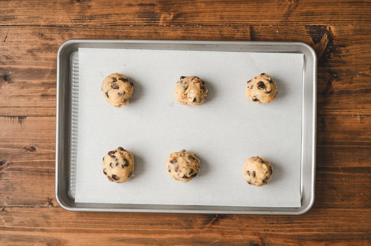 Six cookie dough balls on a parchment lined baking sheet.