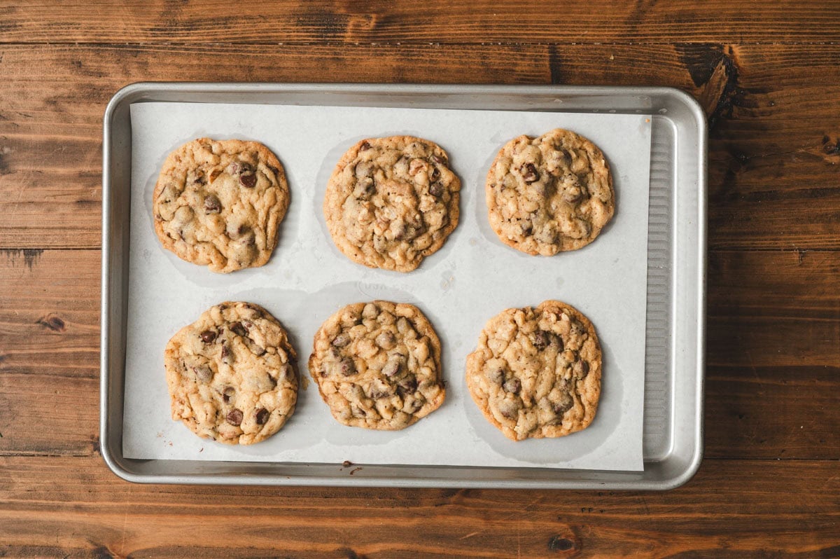 Six large baked chocolate chip cookies on a parchment lined sheet pan.