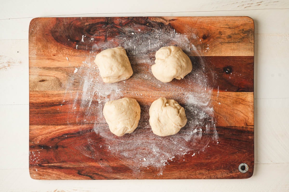 Four balls of bread dough on a flour dusted wooden board.