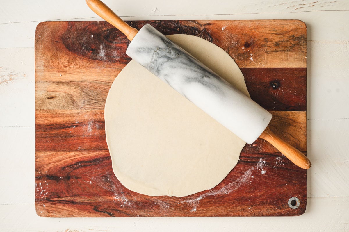 Star bread dough rolled out into a flat shape on a wooden board with rolling pin.