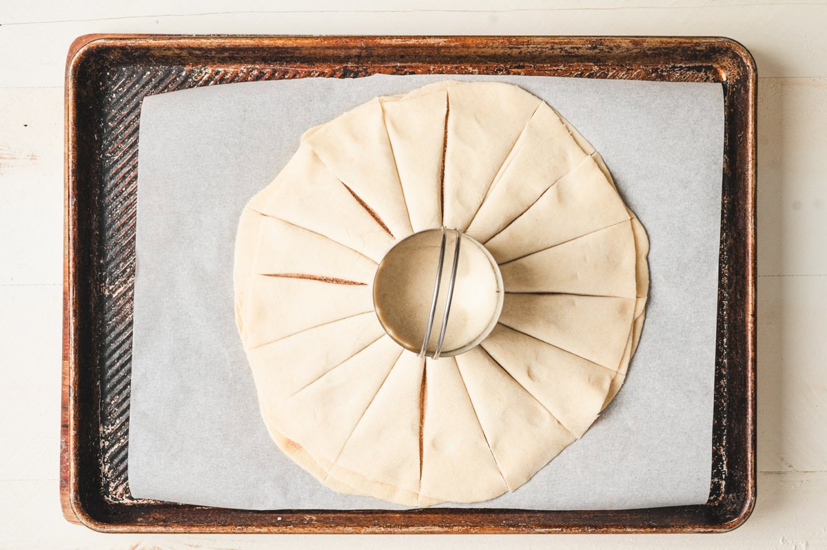 Thin circles of dough stacked with a round biscuit cutter in the center and cuts from center to the edge.