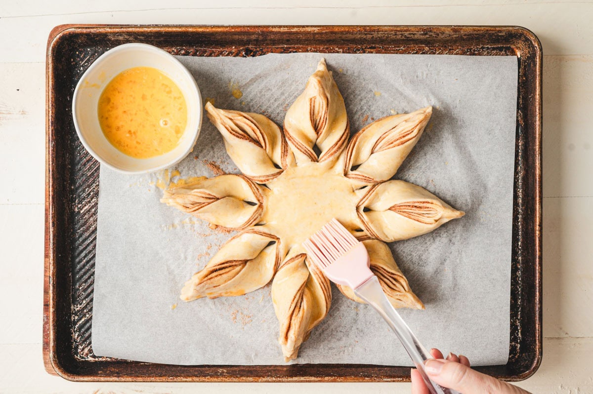 Unbaked cinnamon star bread dough being brushed with egg wash.