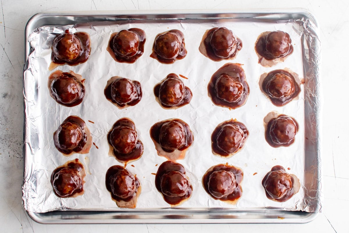 baked meatballs on a foil lined sheet pan covered with bbq sauce