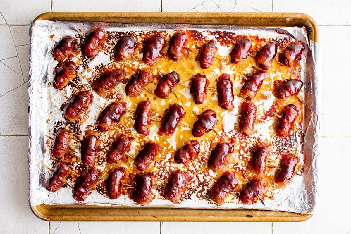 BBQ glazed bacon wrapped little smokies on a foil lined sheet pan.