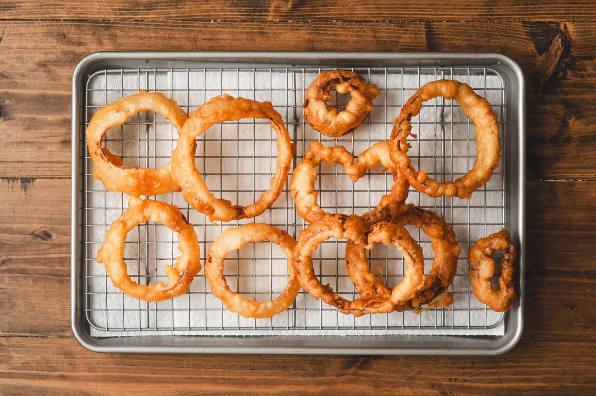 Fried onion rings sitting on a wire rack.