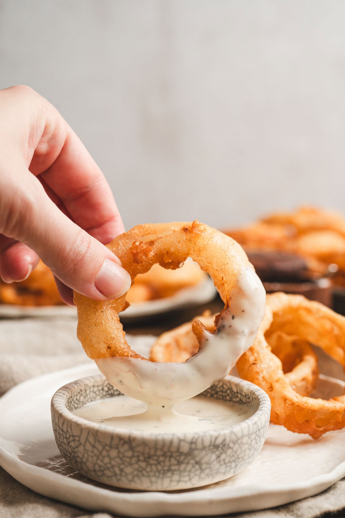 Hand dipping a fried onion ring in sauce.