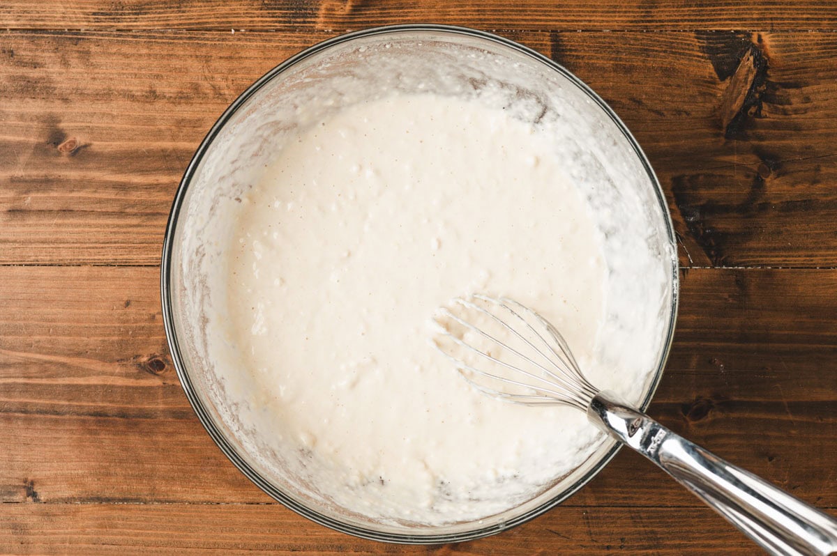 Beer batter for onion rings being whisked in a glass bowl.