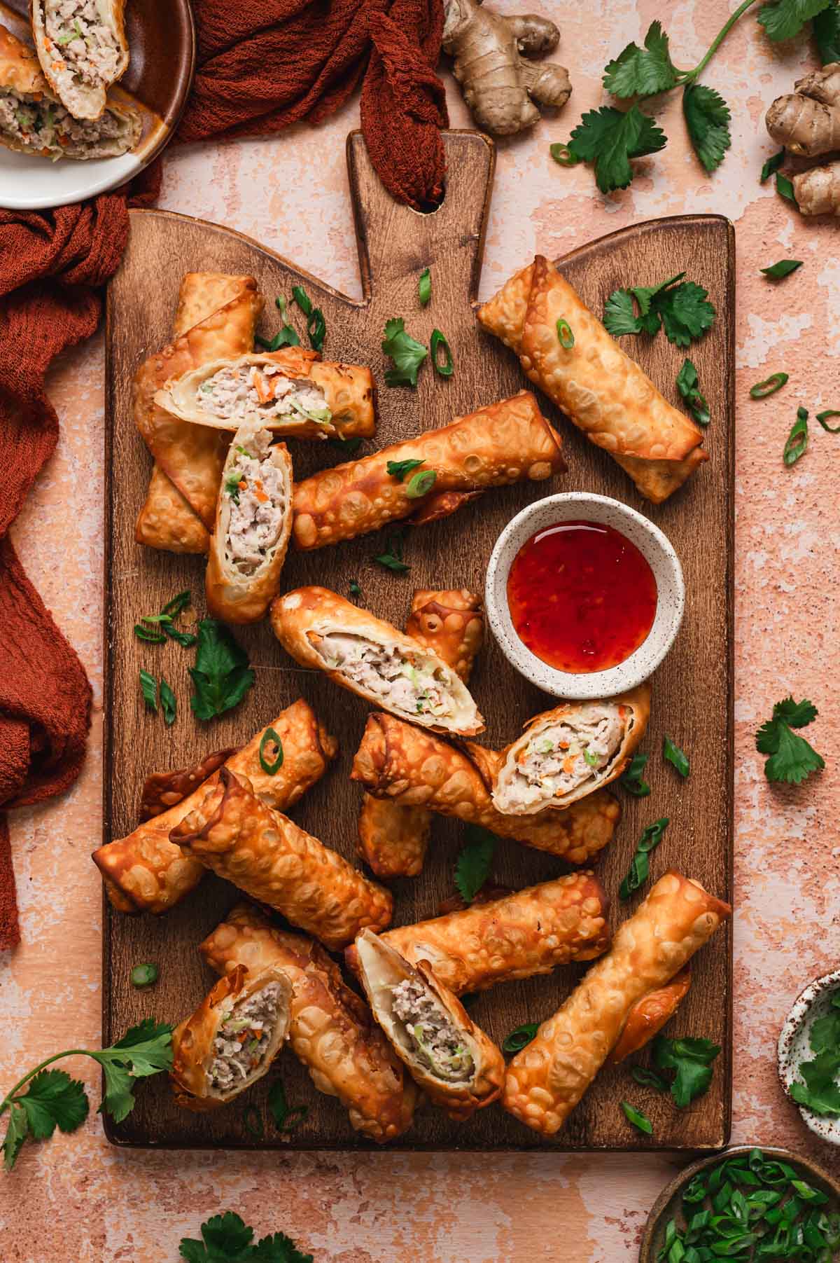 Pork egg rolls on a wooden board with chili sauce in a ceramic dish.