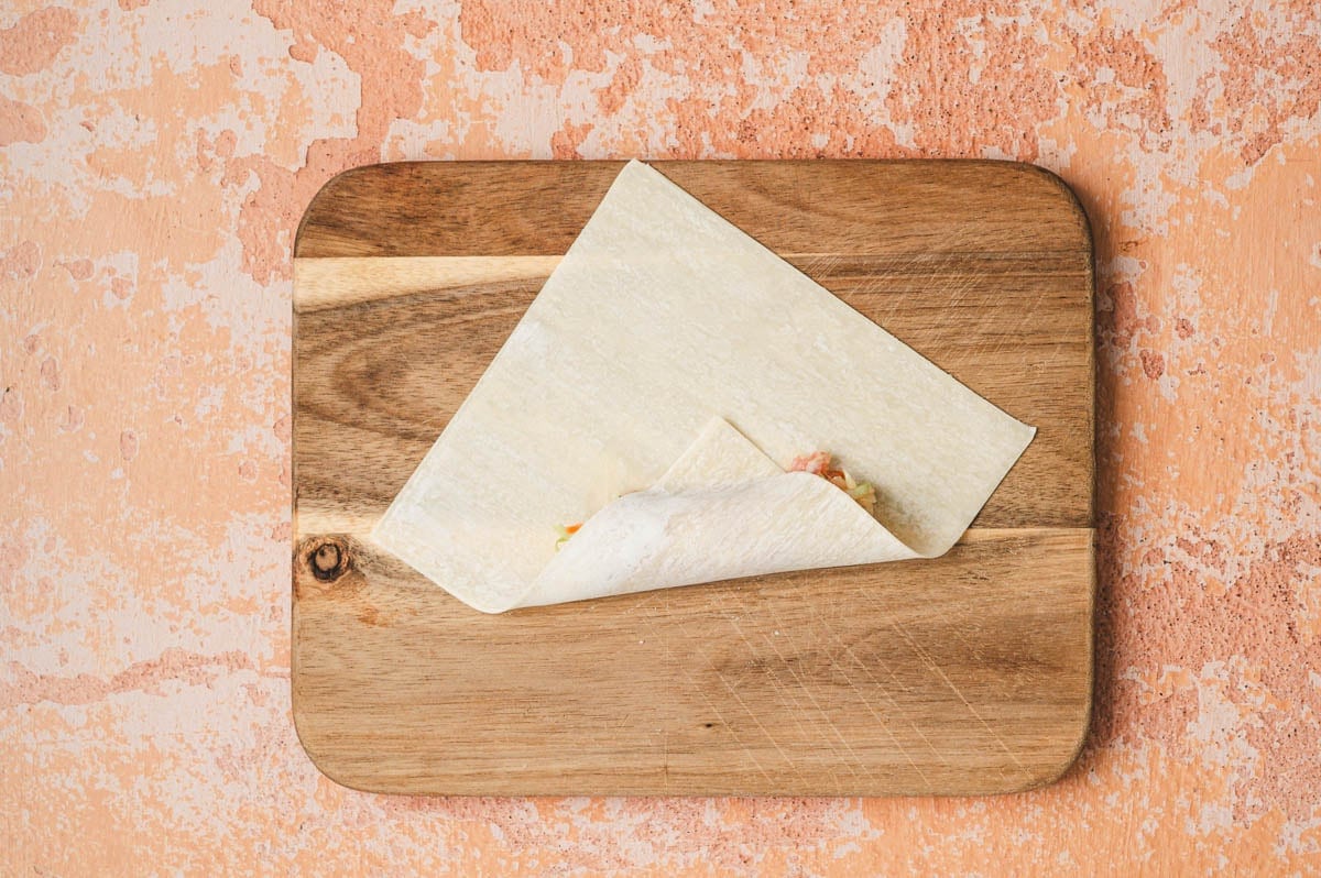 Egg roll wrapper with pork and vegetable filling being rolled up.