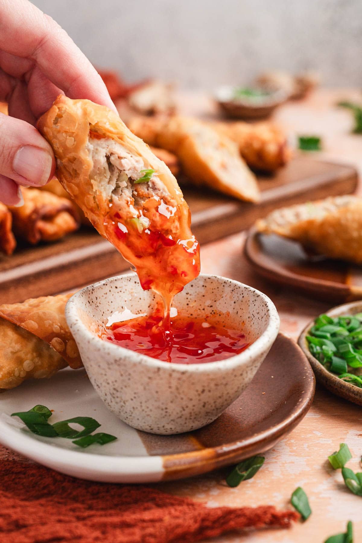 Pork egg roll being dipped in chili sauce.