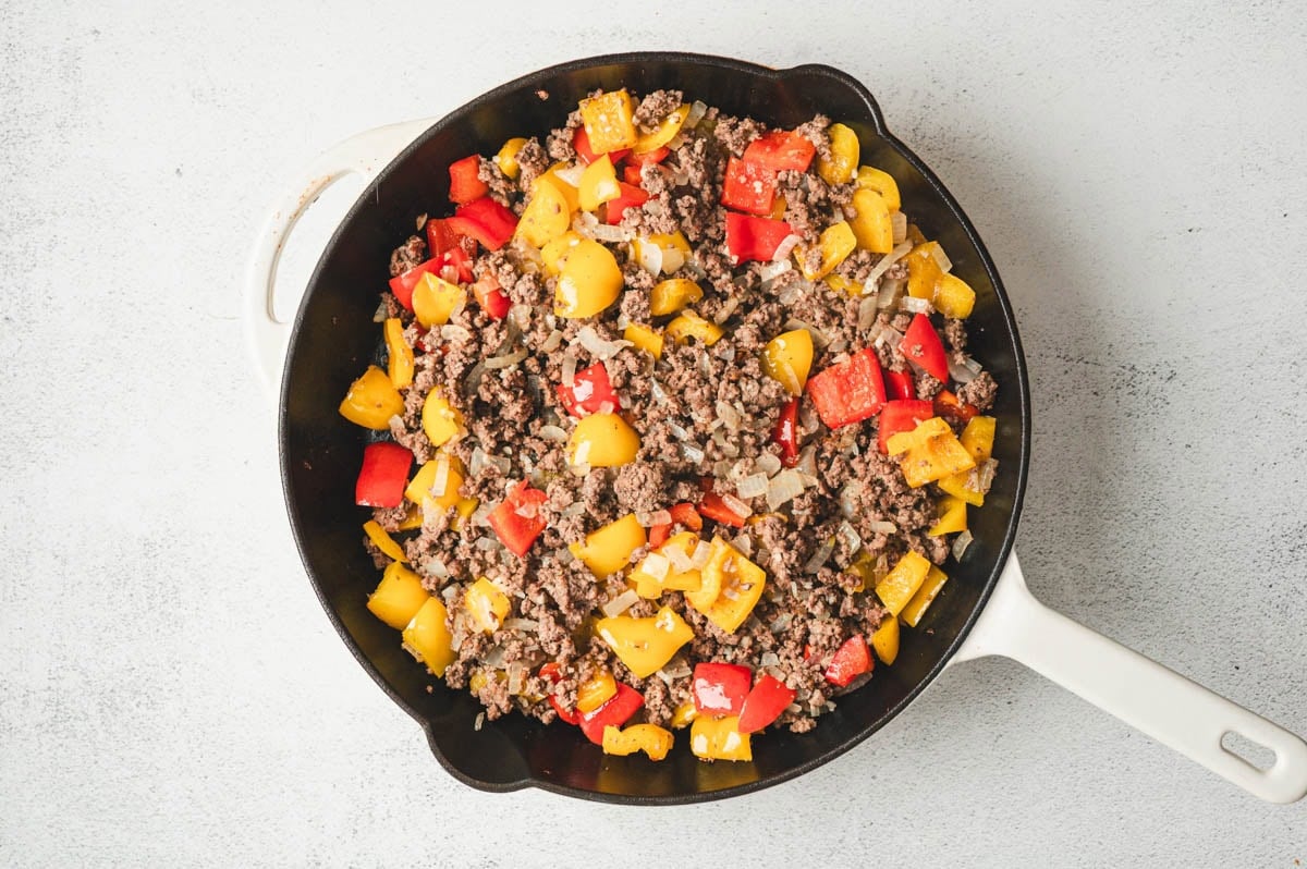Ground beef with yellow and red bell peppers in a skillet.