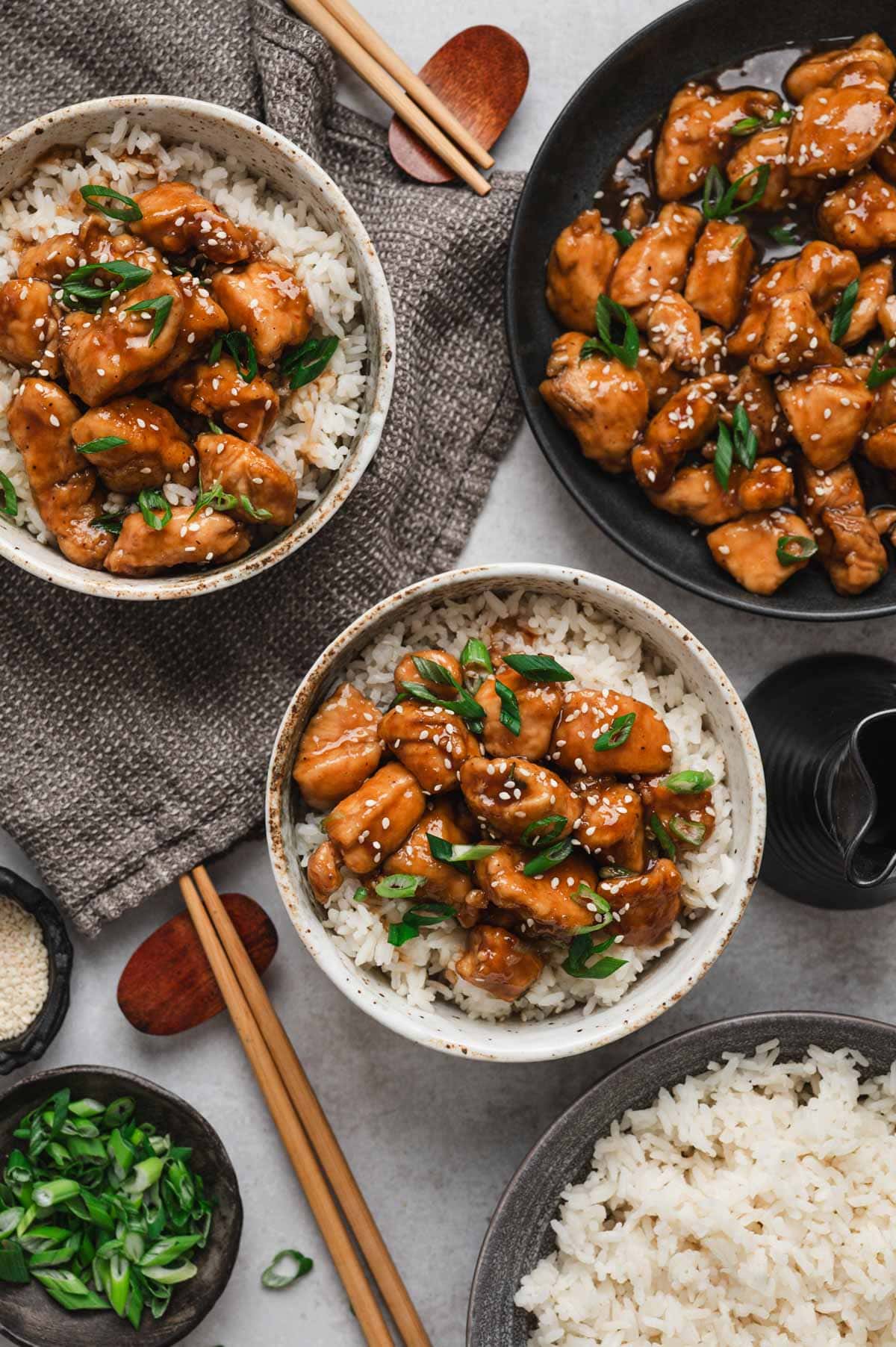 Bowls of bourbon chicken served over rice with sliced green onions on top.