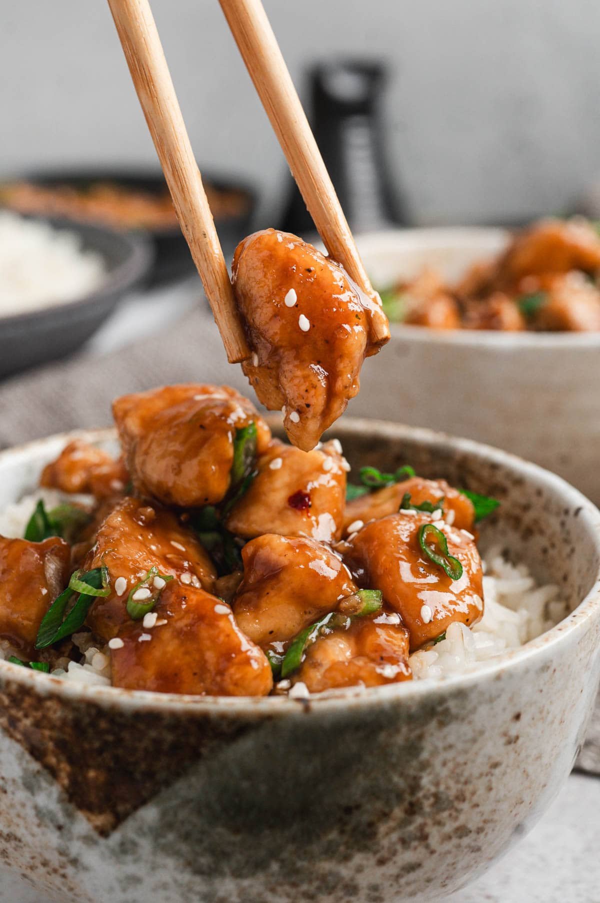 Close up of bourbon chicken served over rice with sliced green onions on top.