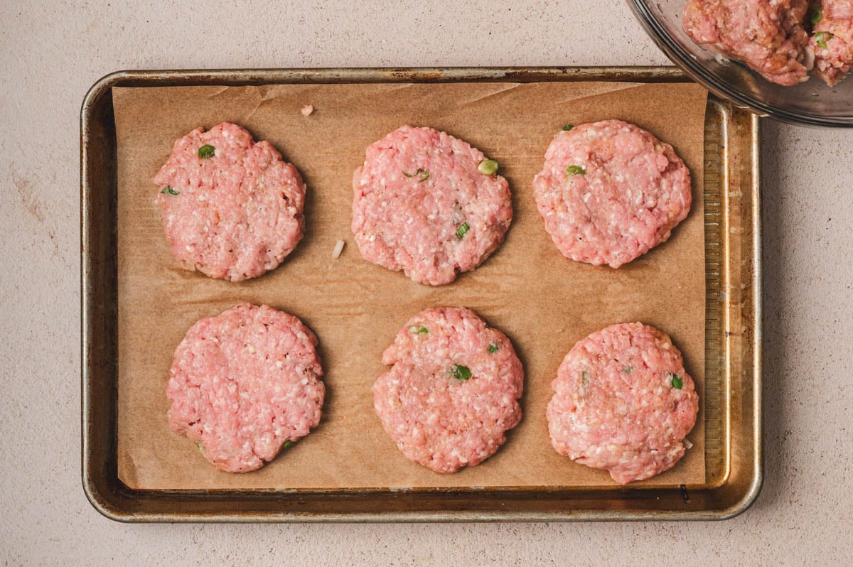 Ground pork patties (uncooked) on a parchment lined sheet pan.