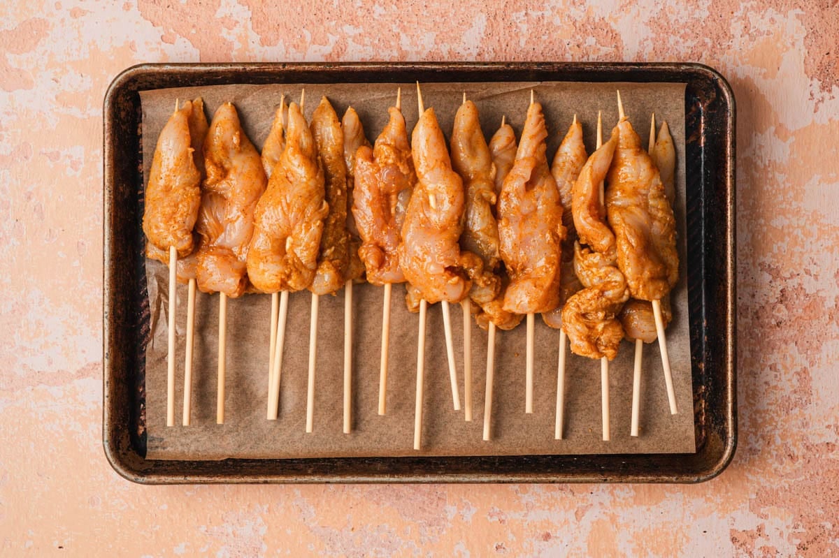 Uncooked chicken satay threaded on wooden skewers.