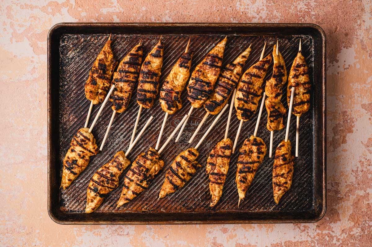 Grilled chicken satay on wooden skewers on a sheet pan.
