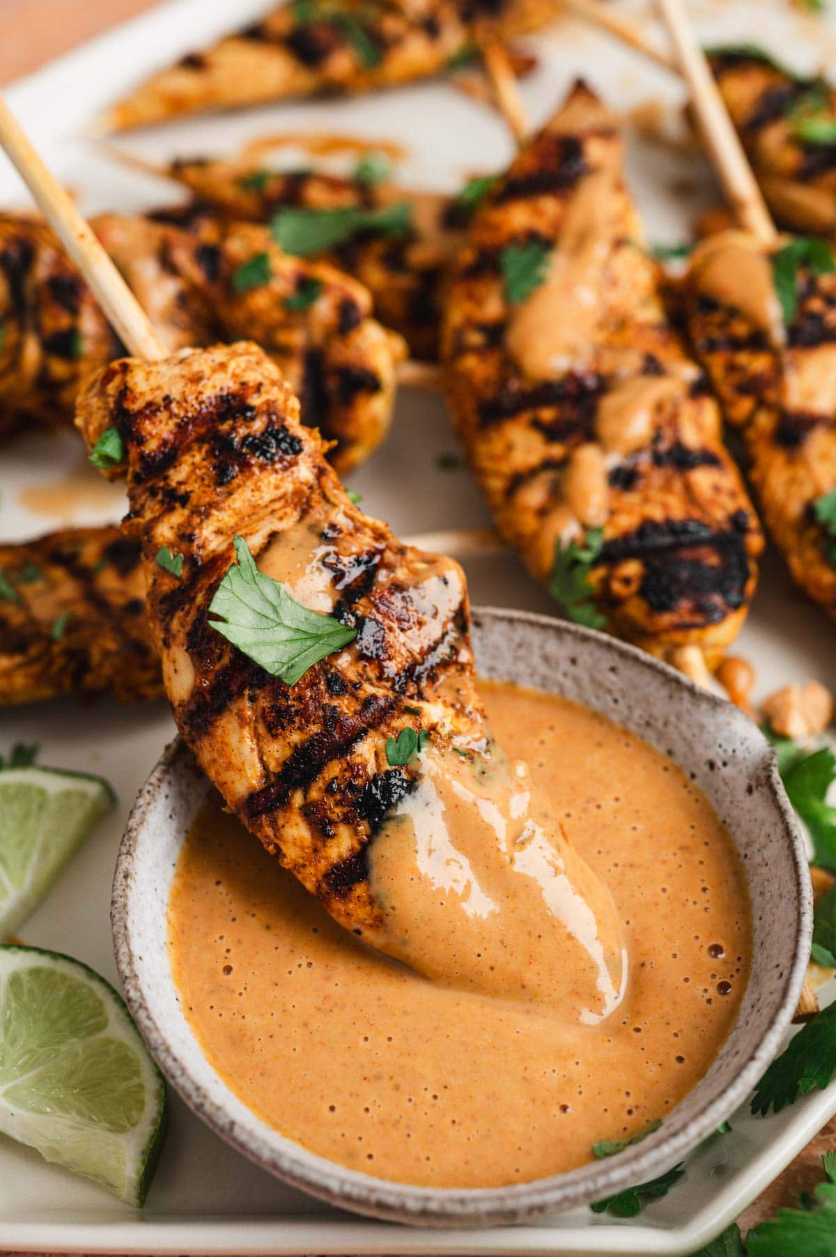 Close up of chicken satay on a skewer dipped in peanut sauce, garnished with cilantro