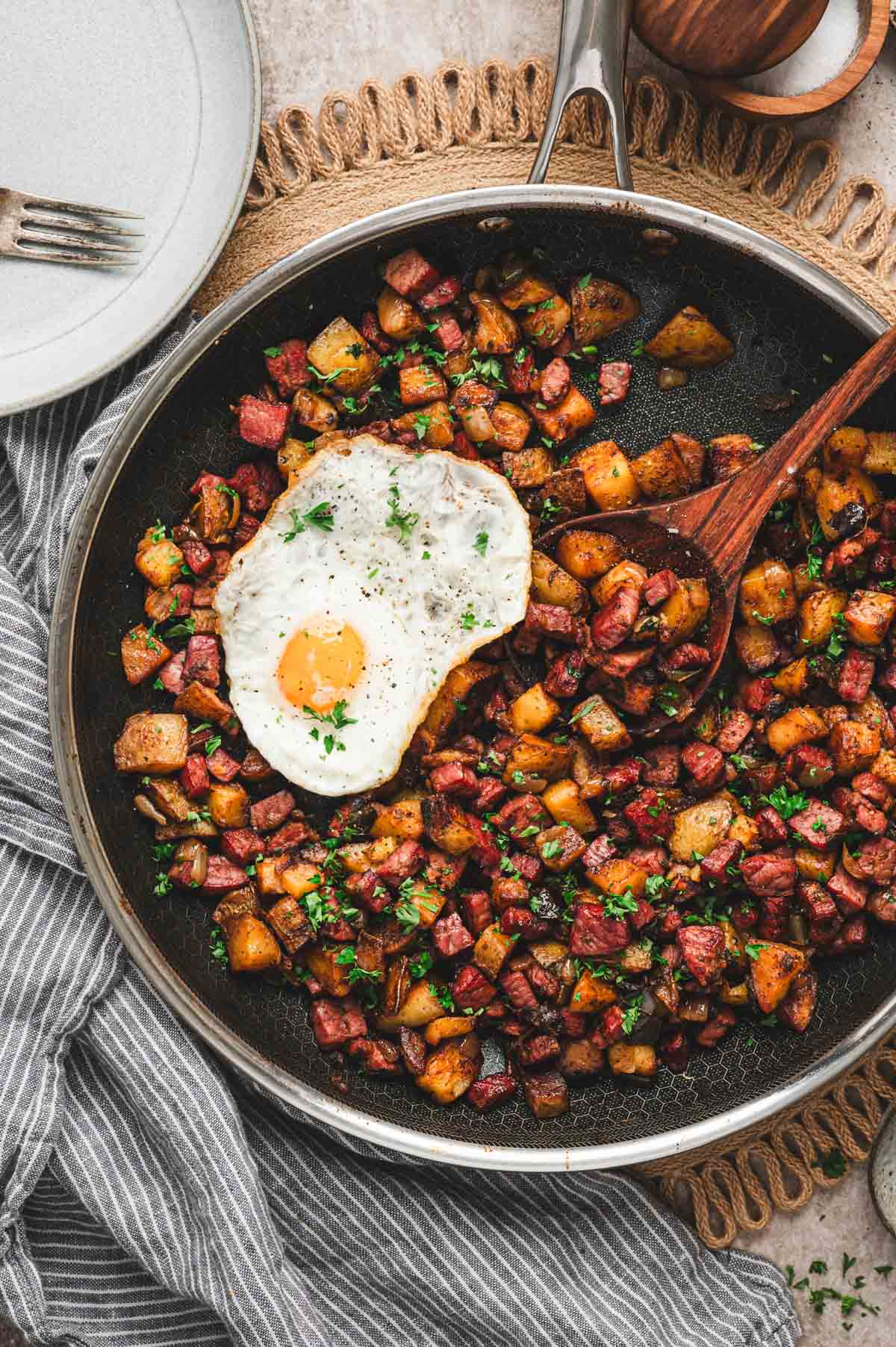 Corned beef hash and diced potatoes in a skillet with egg and chopped parsley on top.