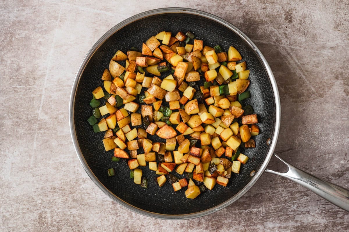 Diced cooked potatoes and green onion in a skillet.