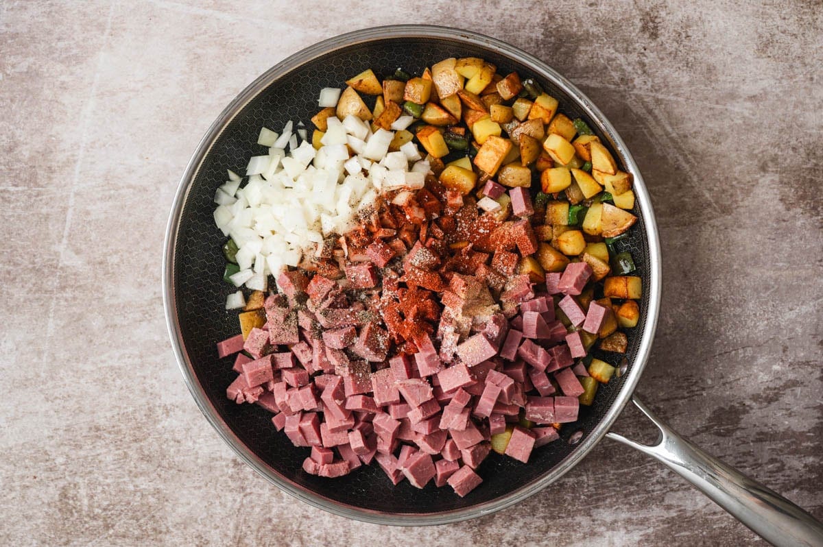 Cooked potatoes in a skillet with onion, diced corned beef and spices in a skillet.