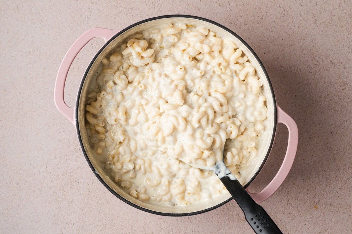 Green chile mac and cheese being stirred in a pot.