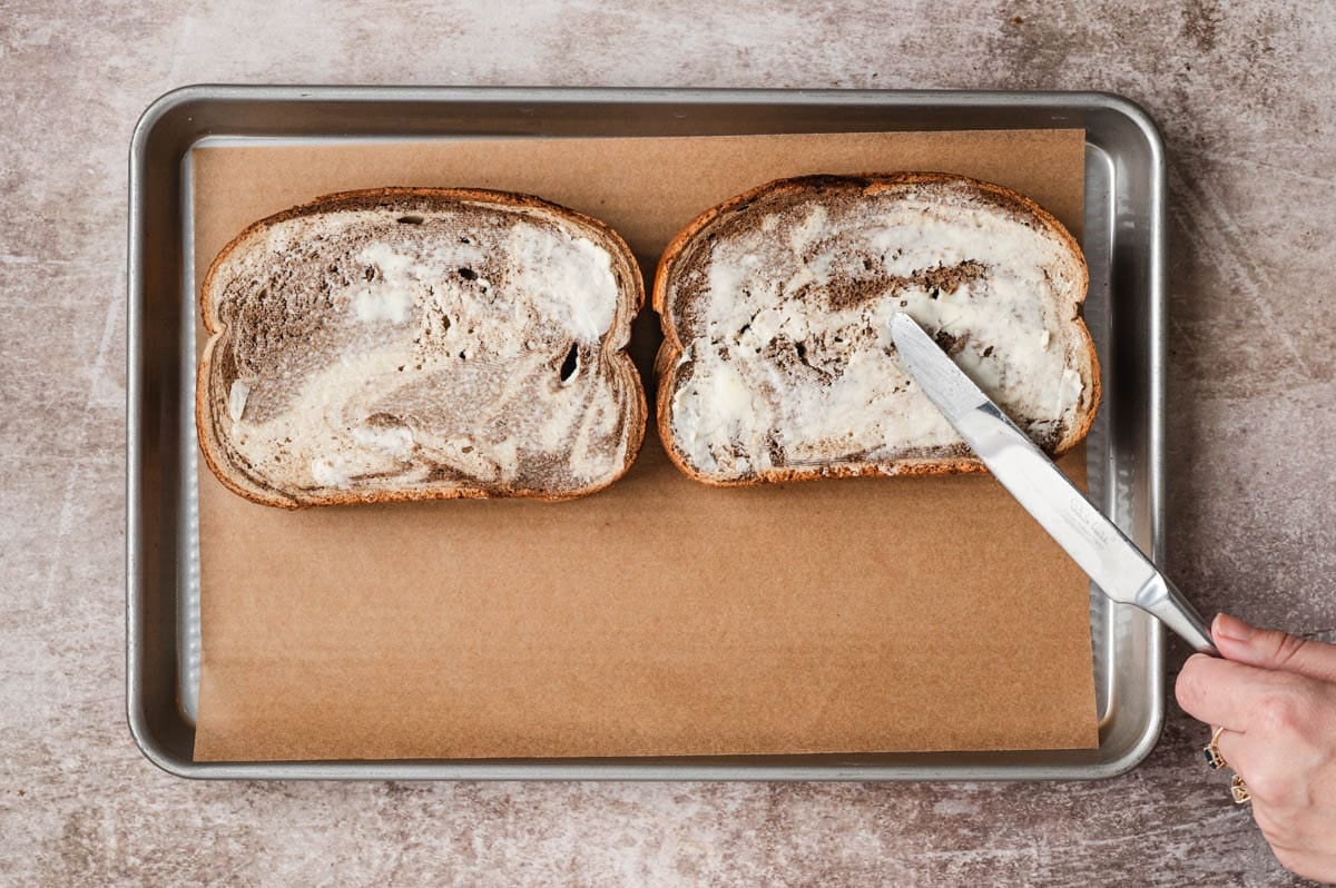 Rye bread with butter being spread on one side.