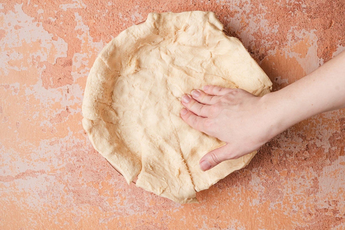 Photo showing a hand making the crescent roll crust for taco pie