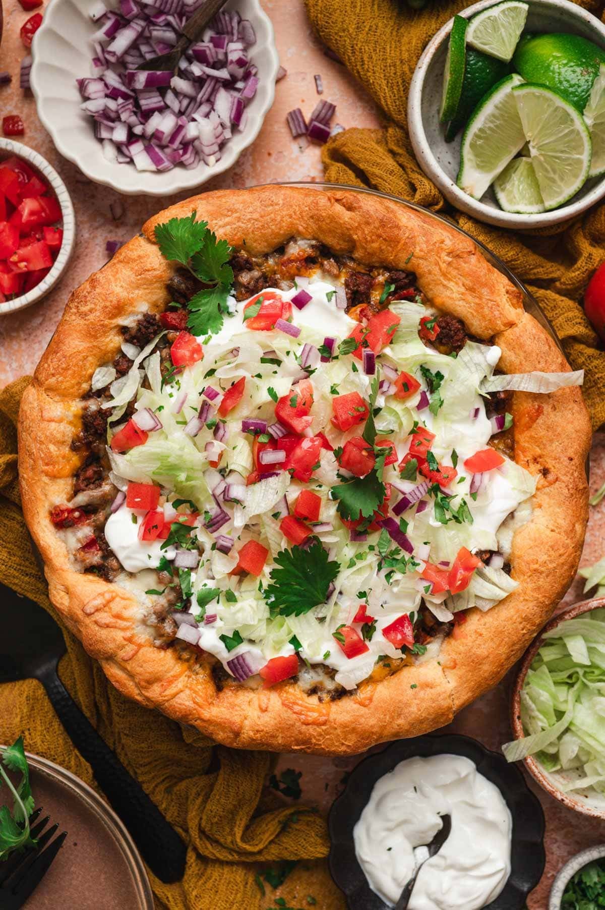 Taco pie with toppings like tomatoes, cilantro, lettuce, sour cream.