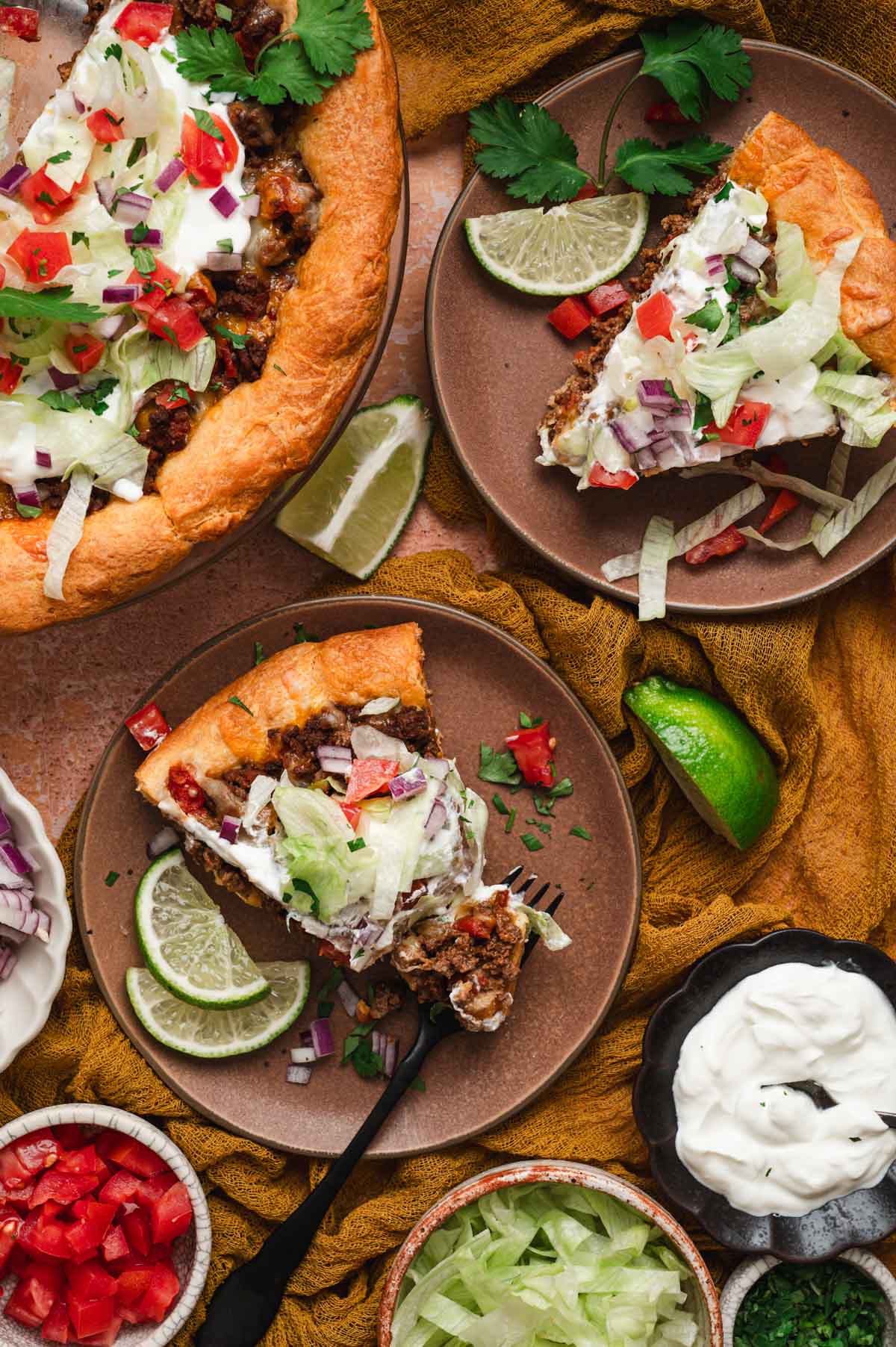 Slices of taco pie on brown plates with lime wedges and sour cream