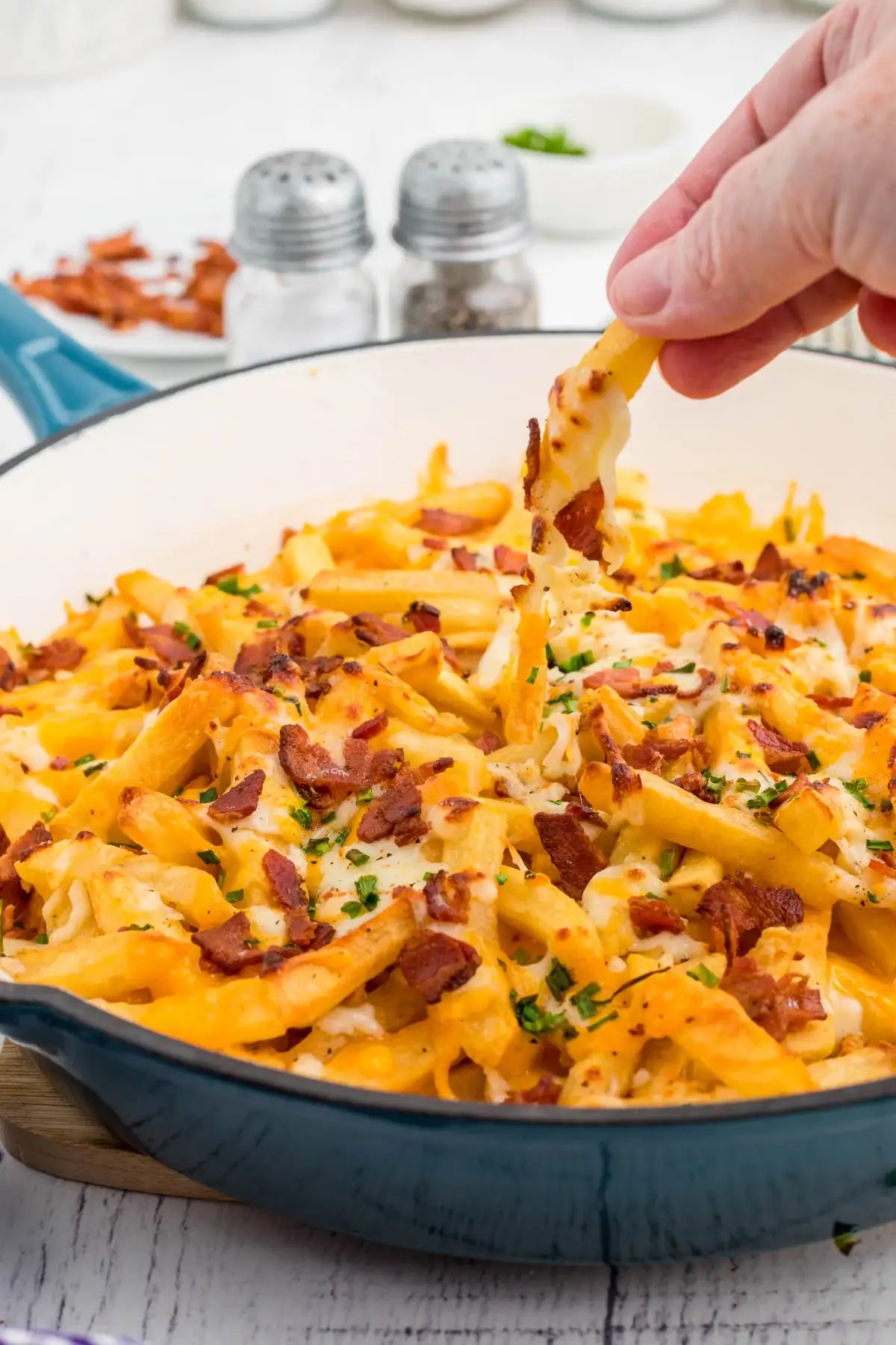 Loaded cheese fries topped with bacon and chives in a blue enameled cast iron pan.