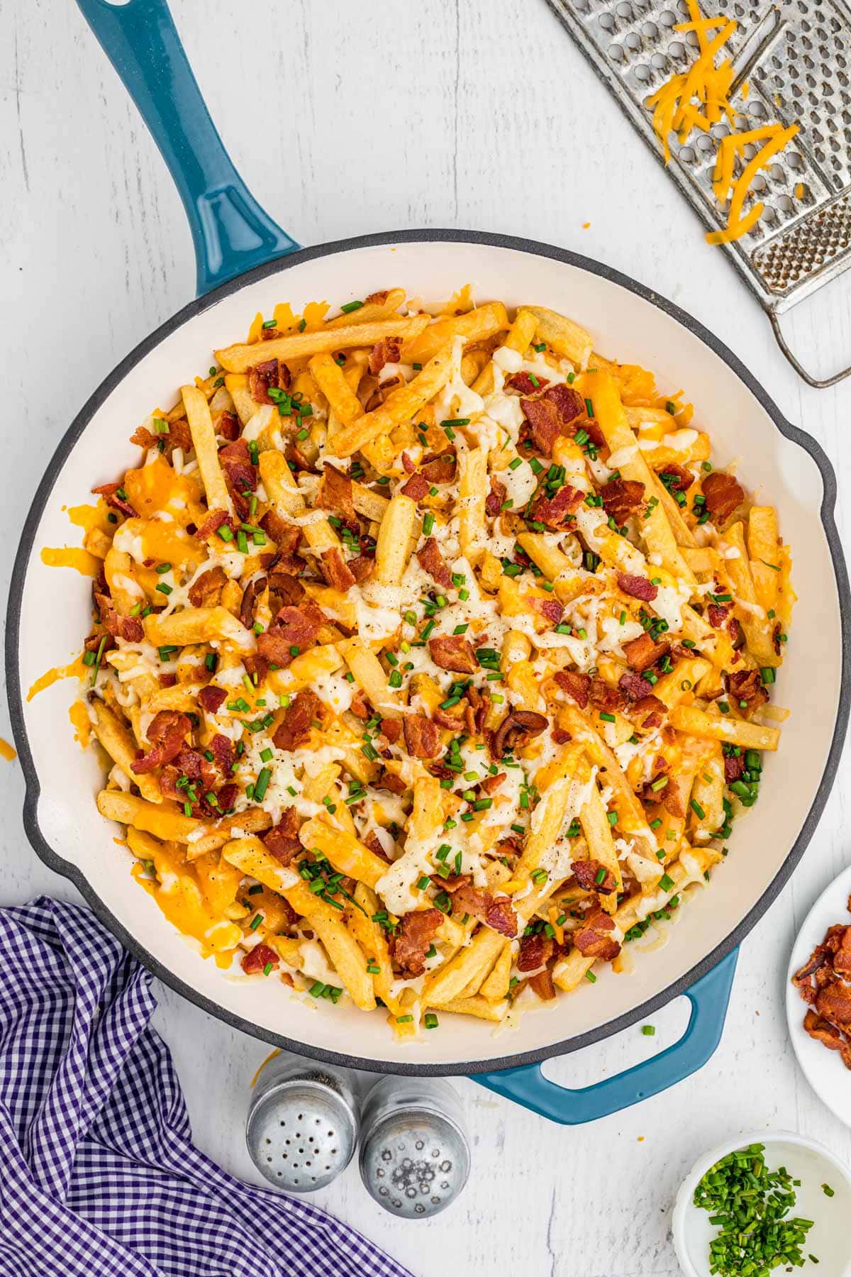 Cheesy fries with bacon and chives in a cast iron pan.