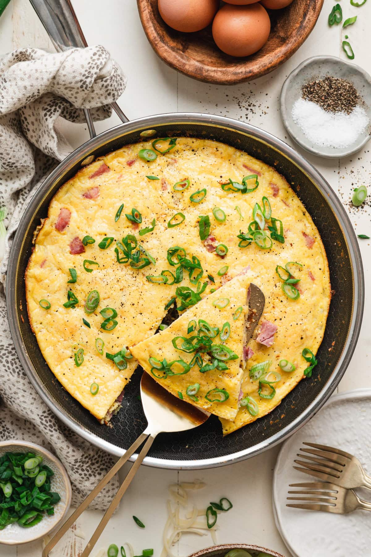 Ham and cheese frittata with green onion garnish in a pan.