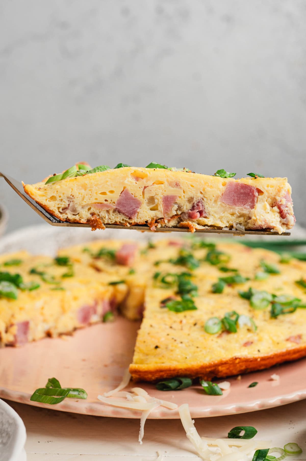 Slice of ham and cheese frittata on a spatula.