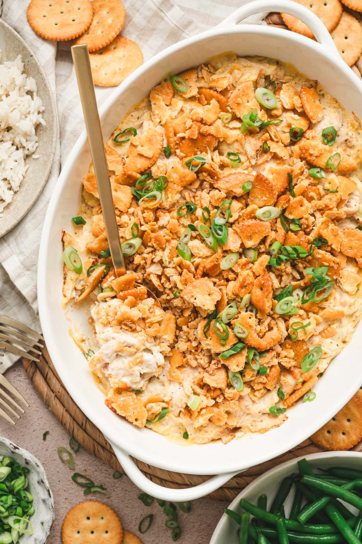 Ritz cracker chicken casserole garnished with green onions in a serving dish with a gold spoon.