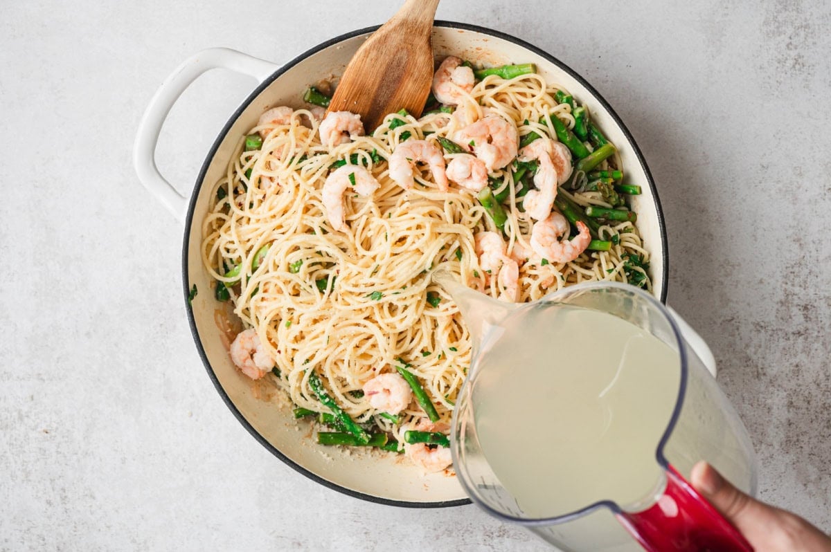 Shrimp and asparagus pasta with pasta water being poured in.