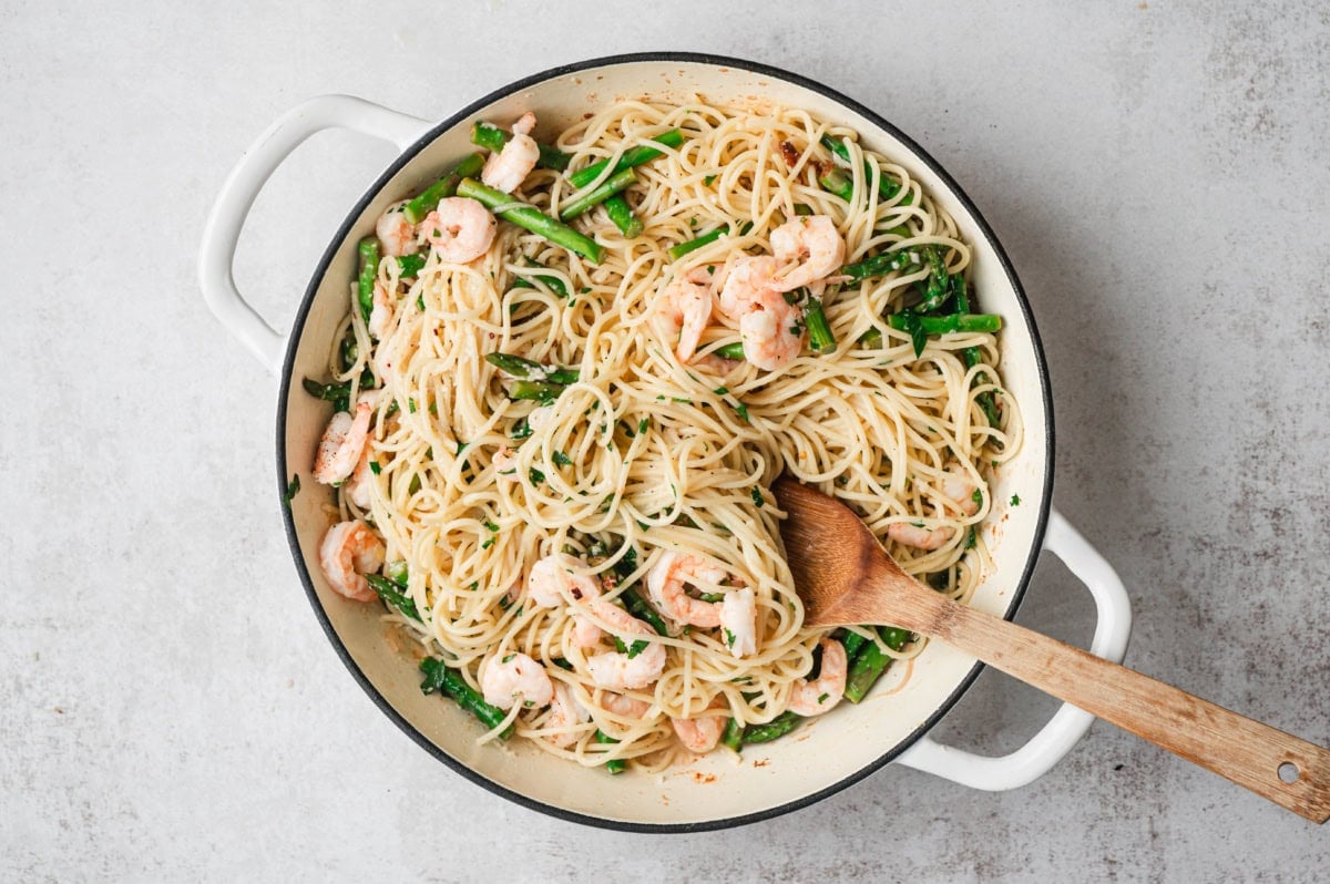 Shrimp and asparagus pasta in a pan with a wooden spoon