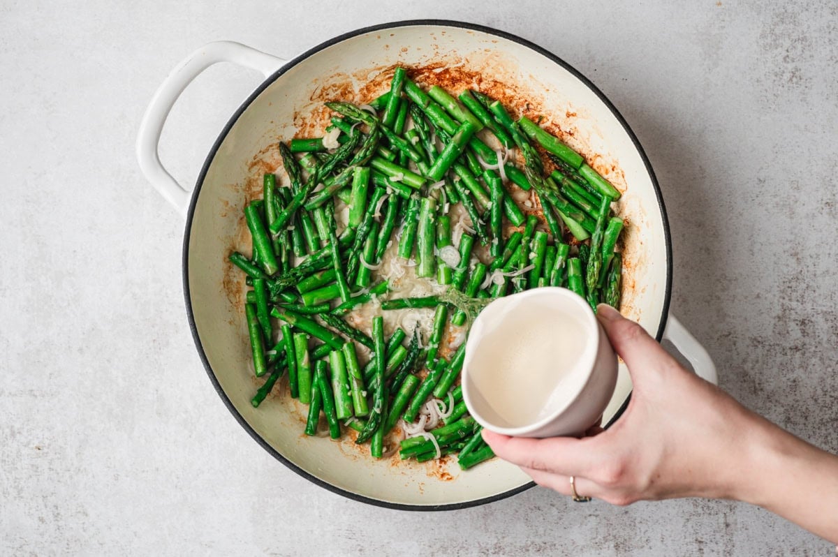 Wine being poured into a saute pan with asparagus and shallots