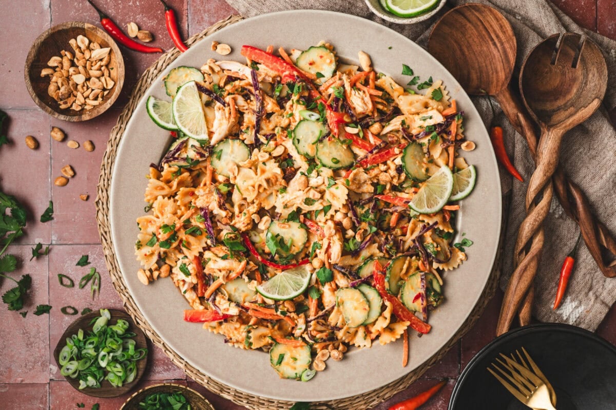 Thai chicken pasta salad garnished with lime slices, green onions, peanuts, and cilantro.