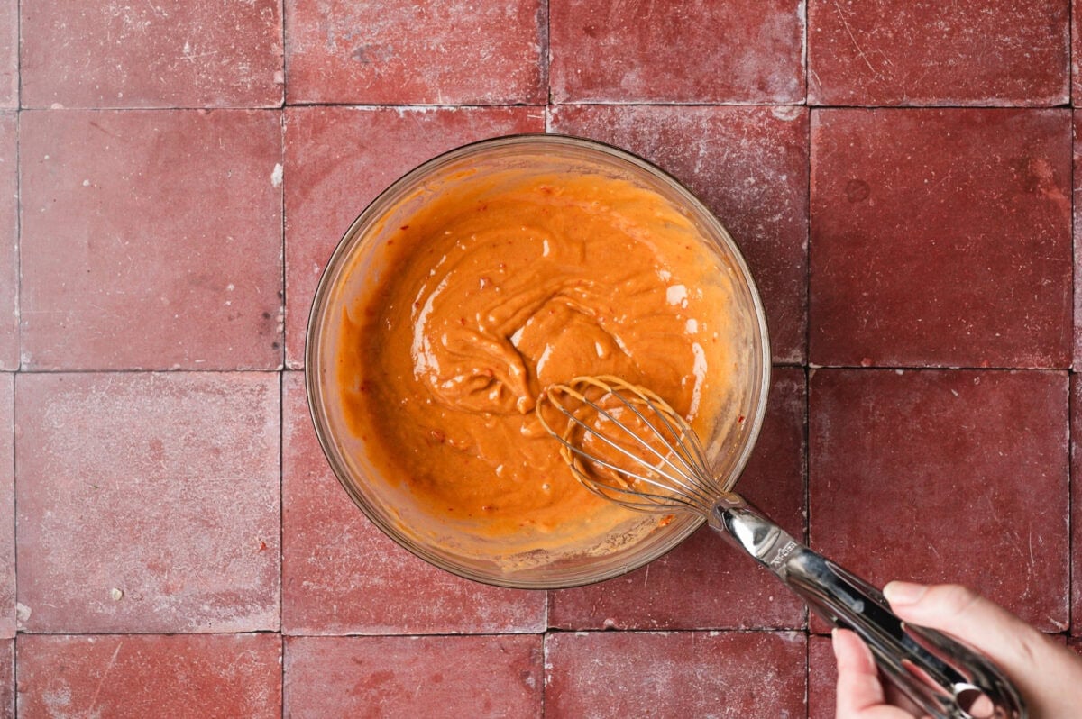 Peanut dressing being whisked in a glass bowl.