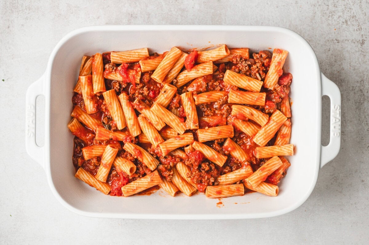 Pasta, marinara sauce and meat in a white casserole dish.