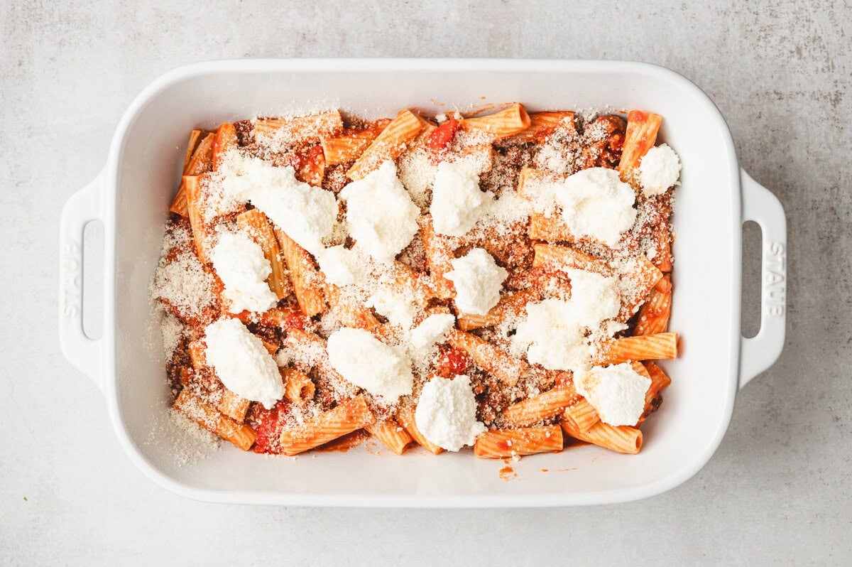 Pasta, meat & tomato sauce, with cheese and ricotta in a white casserole dish.