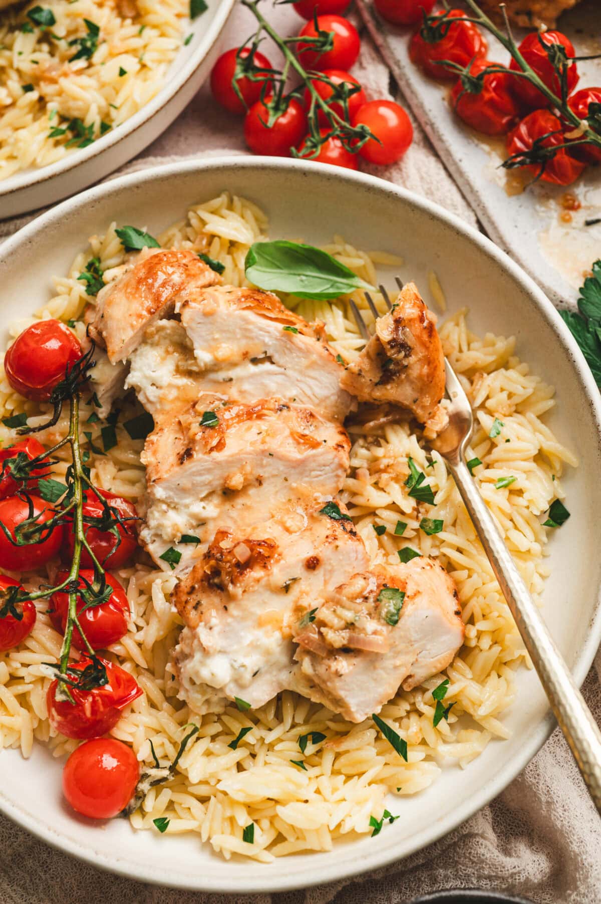 Sliced Boursin stuffed chicken over a plate of orzo with cherry tomatoes.