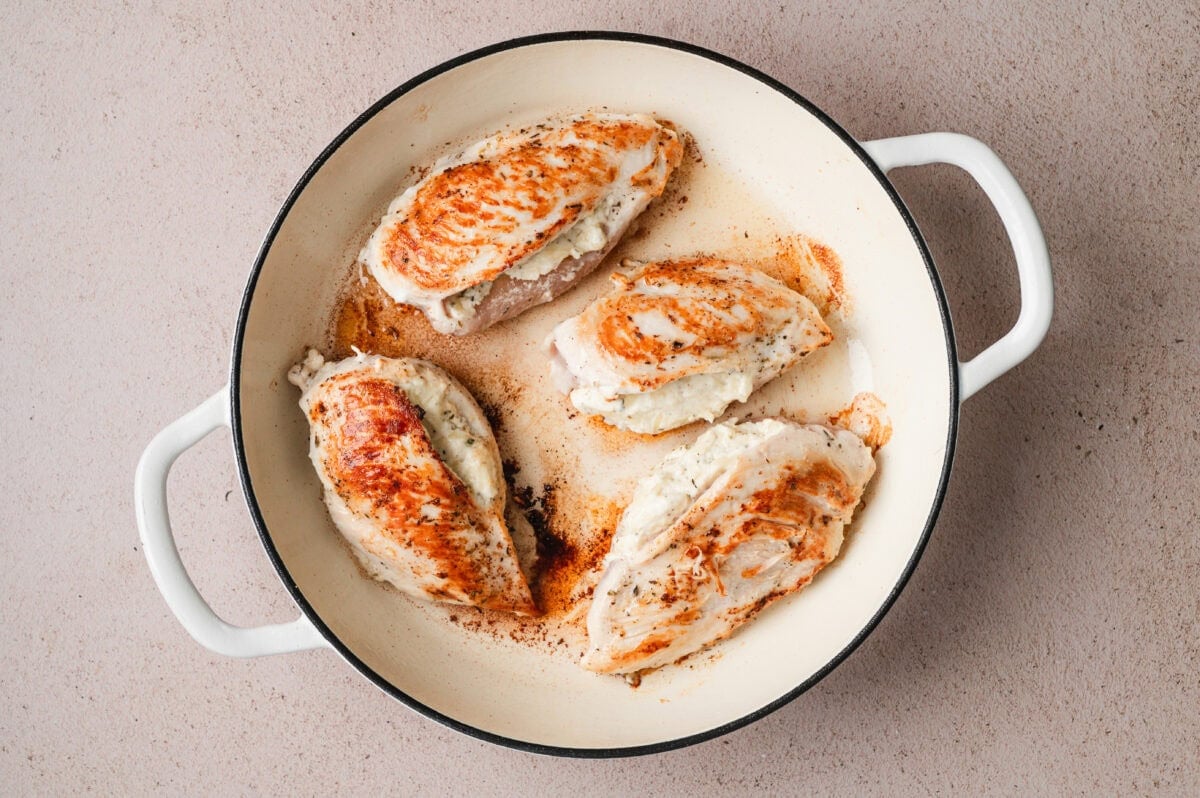 Seared stuffed chicken breasts in a pan.