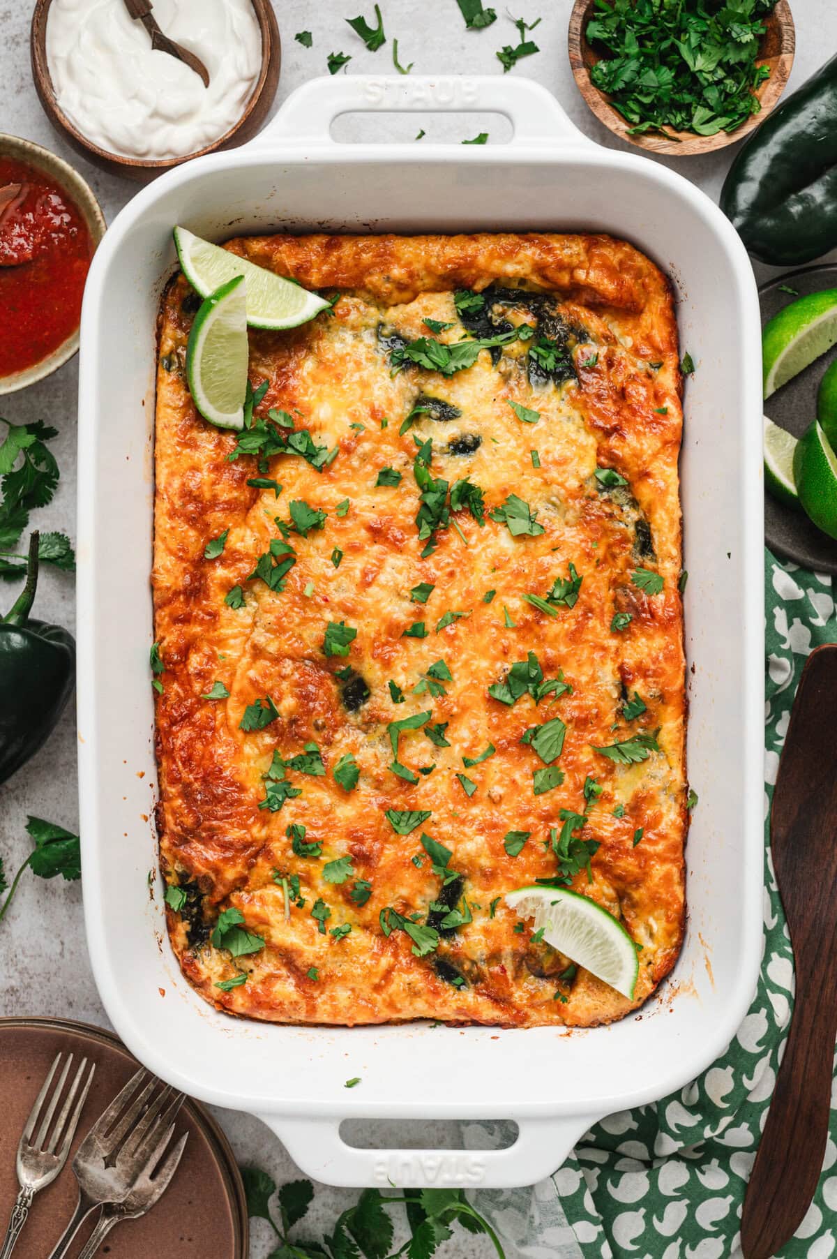 Baked chile relleno casserole in white casserole dish garnished with cilantro and lime wedges